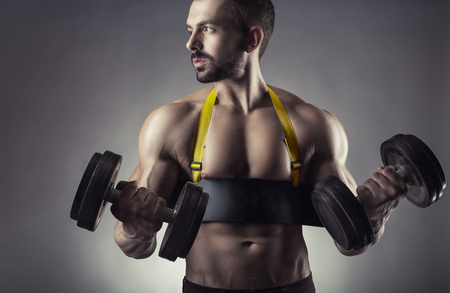 Muscular bodybuilder man exercising with dumbbell on grey backgroundの写真素材