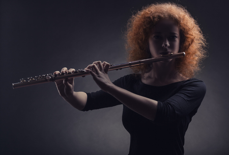 Young beautiful woman playing the flute on black backgroundの写真素材