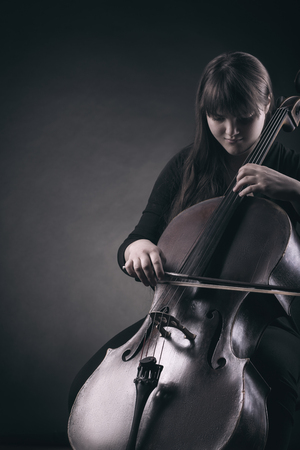 Close-up of cellist playing classical music on cello on black backgroundの写真素材