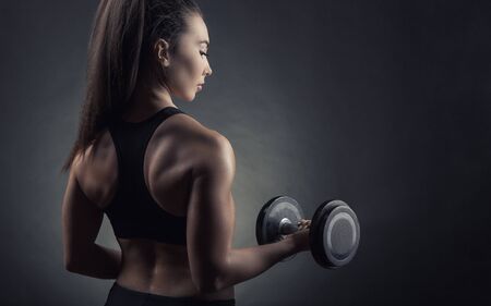 Fitness woman with dumbbells on a dark background. Back view. Sport conceptの写真素材