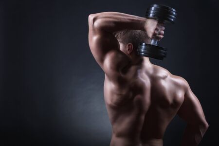 Strong athletic man with dumbbells behind his back on a dark backgroundの写真素材