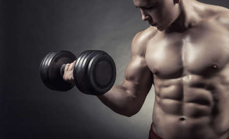 Fit muscular man exercising with dumbbell on dark backgroundの写真素材