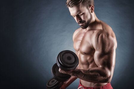 Handsome muscular man exercising with dumbbell on dark backgroundの写真素材