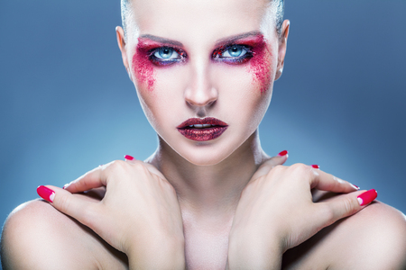 Young woman with fashion makeup and red eye shadows against a blue background. Fashion makeupの写真素材