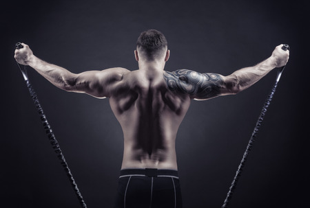 Sports concept. Athletic young man exercising with rubber band against a dark backgroundの写真素材