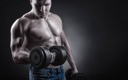 Fit muscular man exercising with dumbbell against a dark backgroundの写真素材