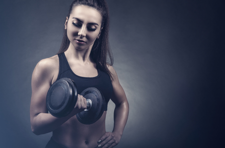 Fitness young woman with heavy weights against a dark backgroundの写真素材