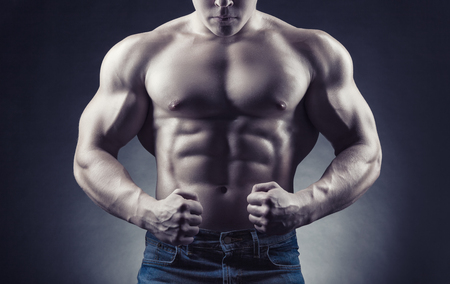 Healthy muscular young man showing his abdominal muscles and strong hands against a dark backgroundの写真素材
