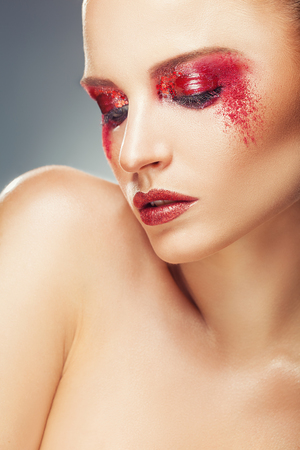 Woman with fashion makeup and red eye shadows. Girl's look pointing down. Fashion makeupの写真素材