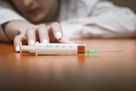 Close-up of a syringe with drugs beside lies a young woman. Focus on the syringeの写真素材