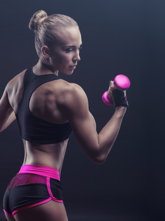 Athletic woman with pink dumbbells against a dark background. Side viewの写真素材