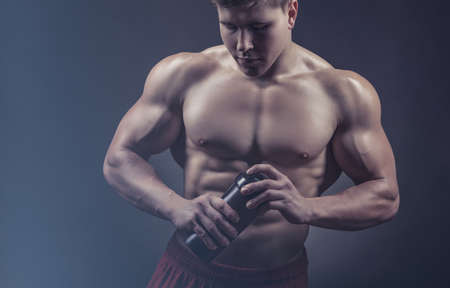 Bodybuilder man after a workout with a shaker against a dark backgroundの写真素材