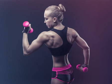 Athletic woman with pink dumbbells against a dark background. Woman showing her sports back
の写真素材