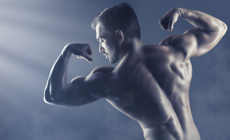 Athletic man shows his muscular back on a dark backgroundの写真素材