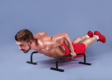 Strong male athlete shows calisthenic moves extended legs planche push ups on parallel bars,  studio shotの写真素材