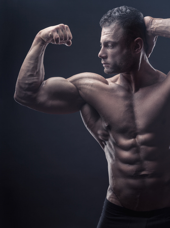 Bodybuilding. Handsome sports man posing in front of the camera on a black background. Shows his pumped-up torso and handsの写真素材