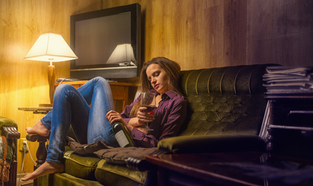 Lonely young woman with a drink rests on the couch in her officeの写真素材