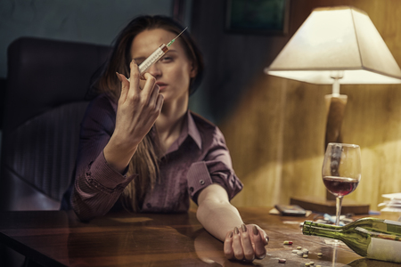 Drug addict young woman with syringe in action in his officeの写真素材
