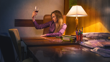 Young beautiful woman in depression, drinking alcohol in the officeの写真素材