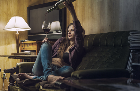 Young beautiful woman pours herself a wine in a glass in her officeの写真素材