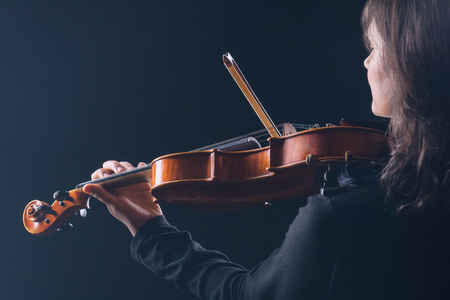 Playing the violin. Woman playing the violin with her back to the camera on a black backgroundの写真素材