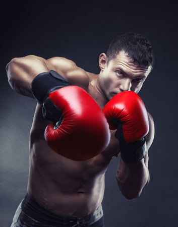 Boxing concept. Boxer with an aggressive look in red boxing gloves before a fight against a black backgroundの写真素材