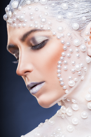 Fantasy make-up. Portrait of beautiful woman with fantasy make-up with white pearls on a dark backgroundの写真素材