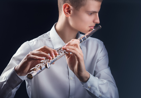 Young man playing the flute on black backgroundの写真素材