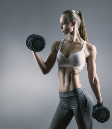 Beautiful fitness woman with heavy weights against a grey background. Sport conceptの写真素材