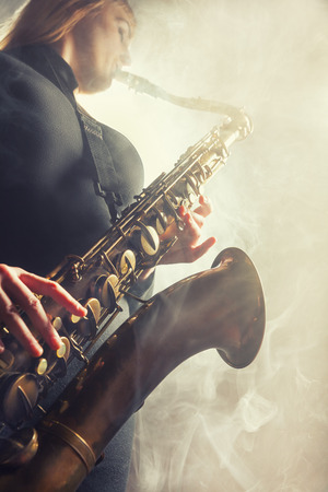 Saxophone player. Woman with saxophone on a beige background. Fog in the background. Studio shotの写真素材