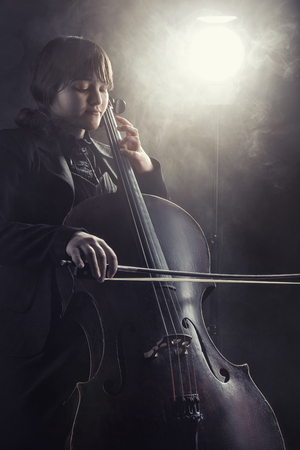 Close-up of cellist playing classical music on cello against a black background. Fog in the background. Studio shotの写真素材