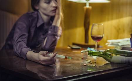 Drug addict young woman with syringe in action in his officeの写真素材