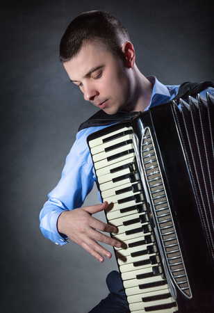 Young man with accordion on a black background. Musical conceptの写真素材