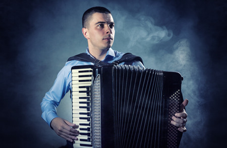 Musician playing the accordion against a black background. Fog in the background. Studio shotの写真素材