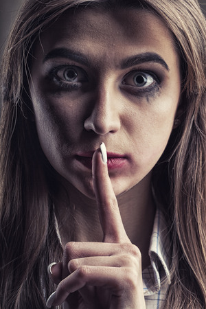 Domestic violence concept. Young woman with finger over her mouthの写真素材