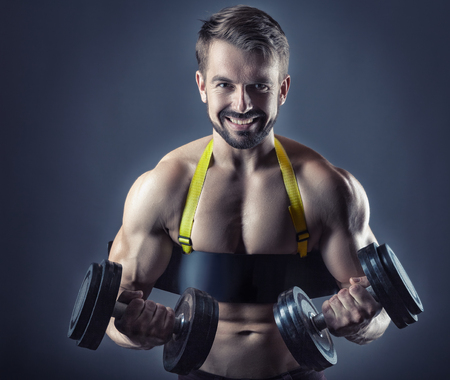 Muscular bodybuilder man exercising with dumbbell on grey backgroundの写真素材