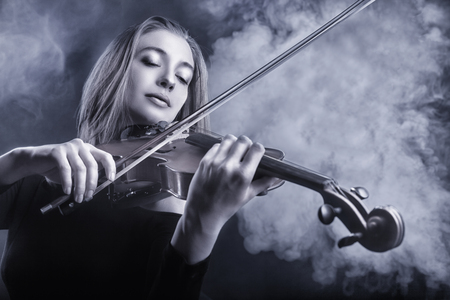 Black and white image. Beautiful young woman playing the violin. Fog in the background. Studio shotの写真素材