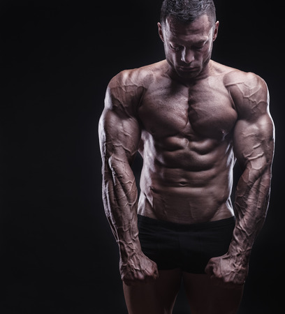 Healthy muscular young man against a dark background. Bodybuilder shows his bodyの写真素材