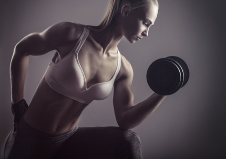 Fitness young woman with heavy weights against a grey backgroundの写真素材