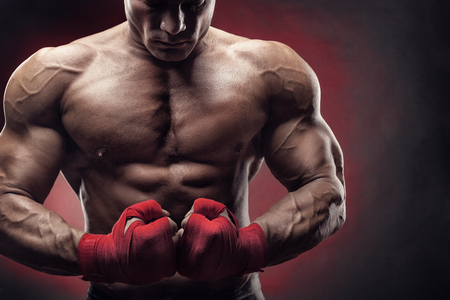 Boxing man ready to fight. Boxer with strong hands and clenched fists in red straps against a black backgroundの写真素材