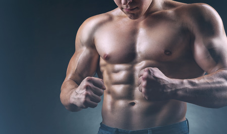 Healthy muscular young man showing his abdominal muscles and strong hands against a dark backgroundの写真素材