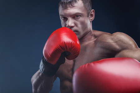 Boxing concept. Boxer with an aggressive look in red boxing gloves before a fight against a black backgroundの写真素材