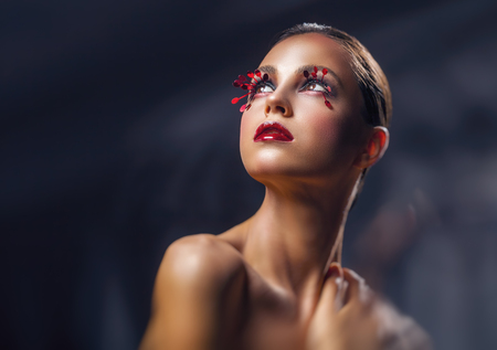 Beautiful young woman with fashion red makeup against a dark background. Female look upの写真素材