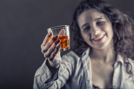 Young woman in depression, drinking alcohol on dark background. Focus on the glass