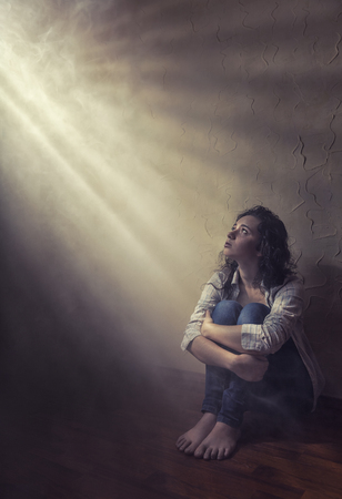 Young sad woman sitting alone on the floor in an empty room in a shadow stripeの写真素材