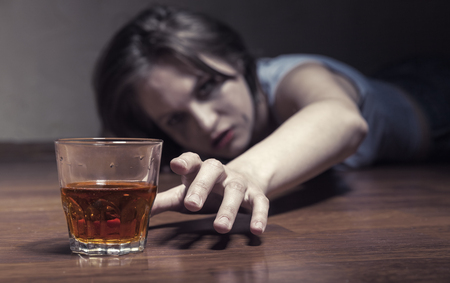 Depressed young woman drinking alcohol while lying on the floorの写真素材