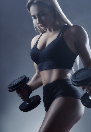 Beautiful sporty woman with heavy weights against a grey background. Sport conceptの写真素材