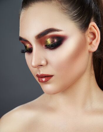 Close up of fashion model young woman in trendy make-up. Eye models with colorful glitter on the eyelids. The gaze of the girl is directed downwardsの写真素材