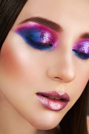 Close-up face of a beautiful sexy fashion woman with closed eyes trendy make-up. Eye models with bright shiny pink and blue eye shadows on the eyelids. Gentle lipsの写真素材