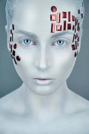 High fashion model. Girl in white makeup and accessories looking at the camera. White skin make-up. Art design makeupの写真素材